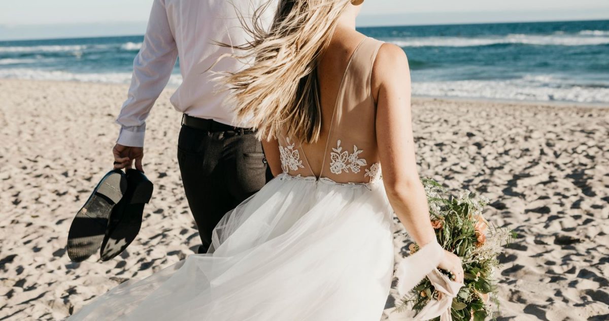 A bride and groom walking together on a sandy beach.